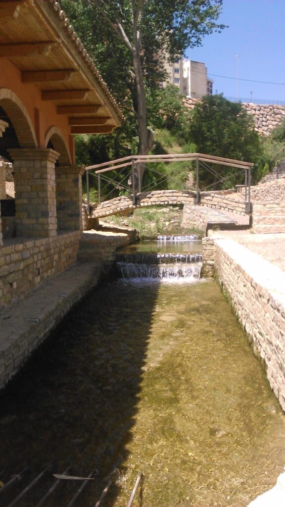 El agua cristalina fluye por un canal de piedra, rodeado por un muro de piedra, en un entorno natural y tranquilo