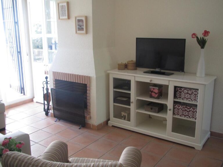 Un salón de un alojamiento en Huelva, con un televisor de pantalla plana, un armario de dos puertas y un hogar de leña
