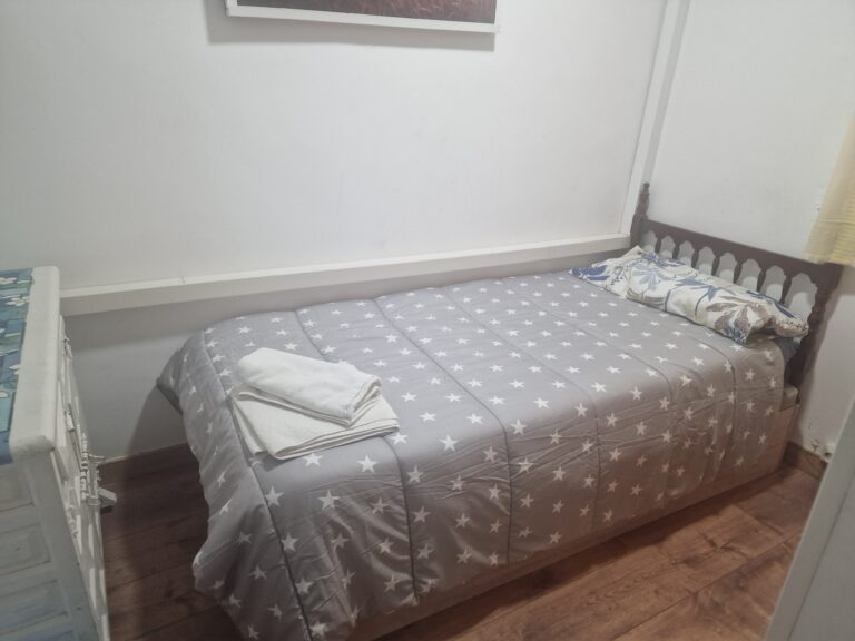 Una cama individual con una cama de madera, una colcha gris con estrellas blancas y dos almohadas con fundas de colores