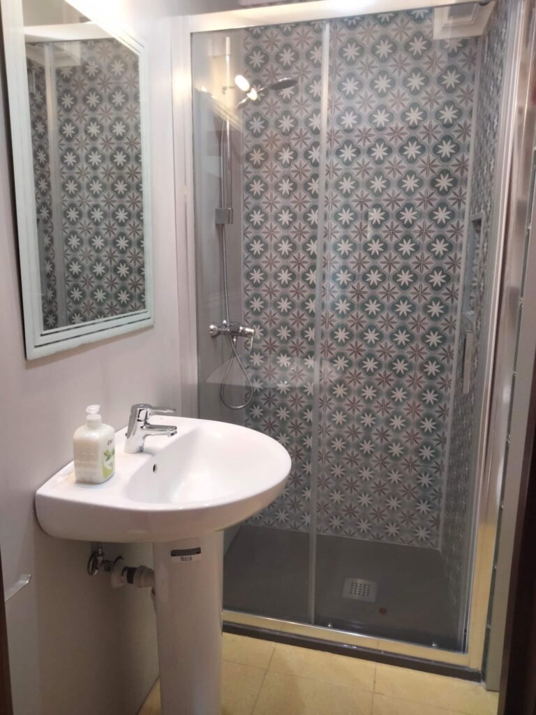 Un baño con una ducha de cristal y un lavabo con un espejo rectangular