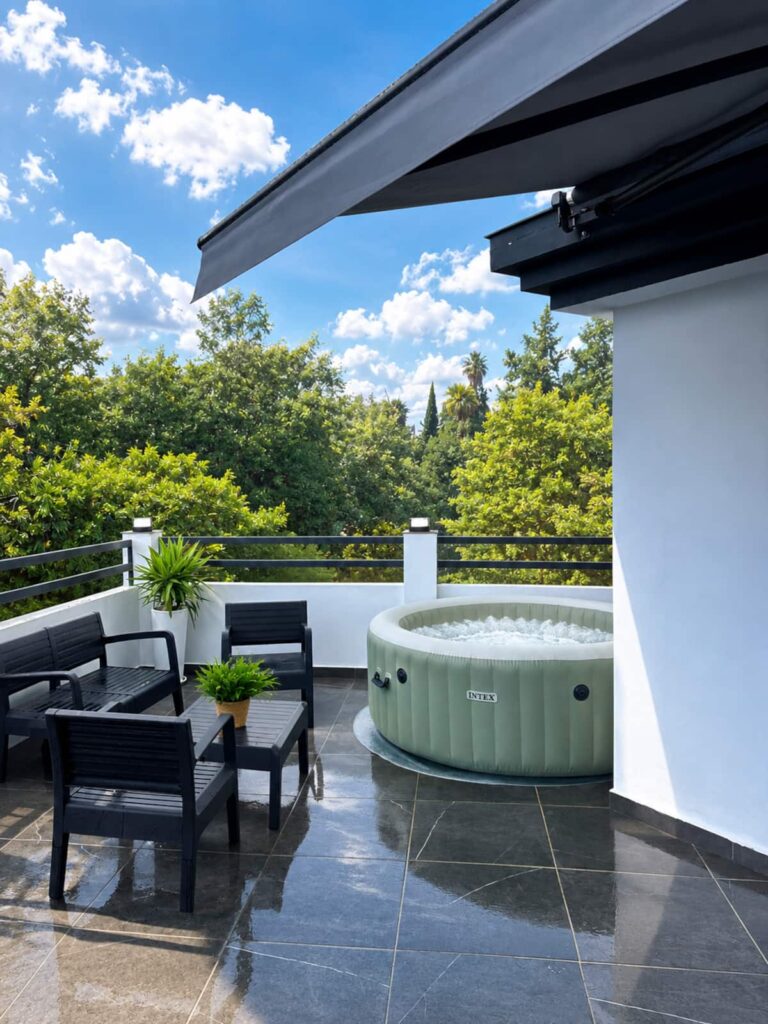 Una terraza con un jacuzzi de color verde claro, rodeado de una pared blanca y una barandilla negra. En el fondo