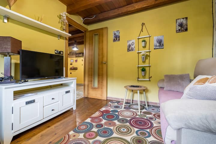 Un salón de un alojamiento en Cantabria, con un sofá de color rosa claro, una mesa de madera y un televisor de pantalla