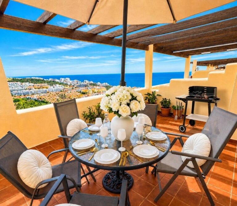 Una terraza con vista a la ciudad de Málaga, con una mesa de comedor circular, cuatro sillas, un vaso de flores
