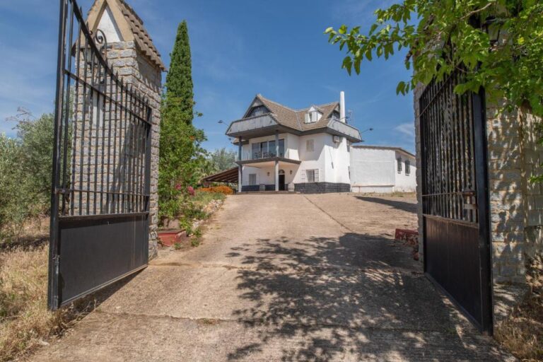 Una casa de dos pisos con un camino de entrada y un jardín. La casa tiene un techo de tejas y una fachada blanca