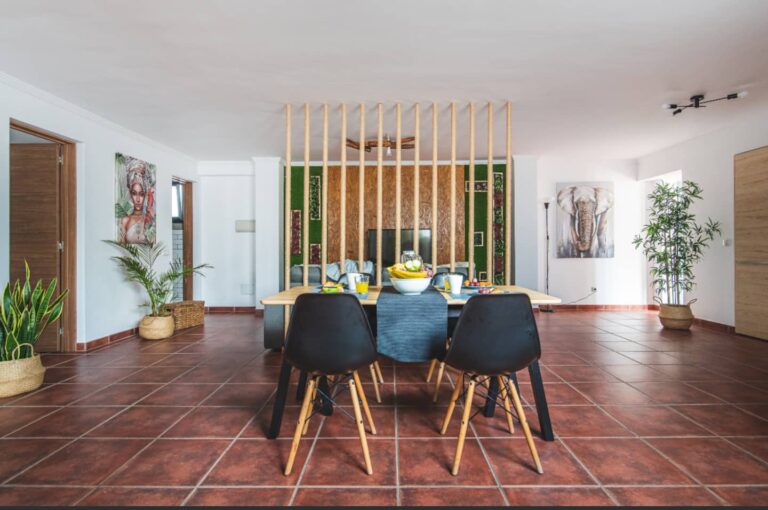 Una mesa de comedor con cuatro sillas negras y madera, en un salón con paredes blancas y piso de terracota