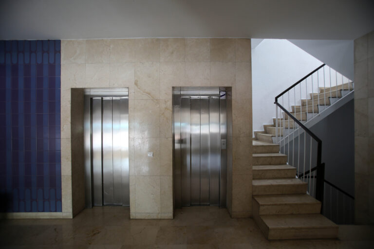 Este es un pasillo interior de un alojamiento ubicado en Sevilla, con dos ascensores de metal y paredes de piedra