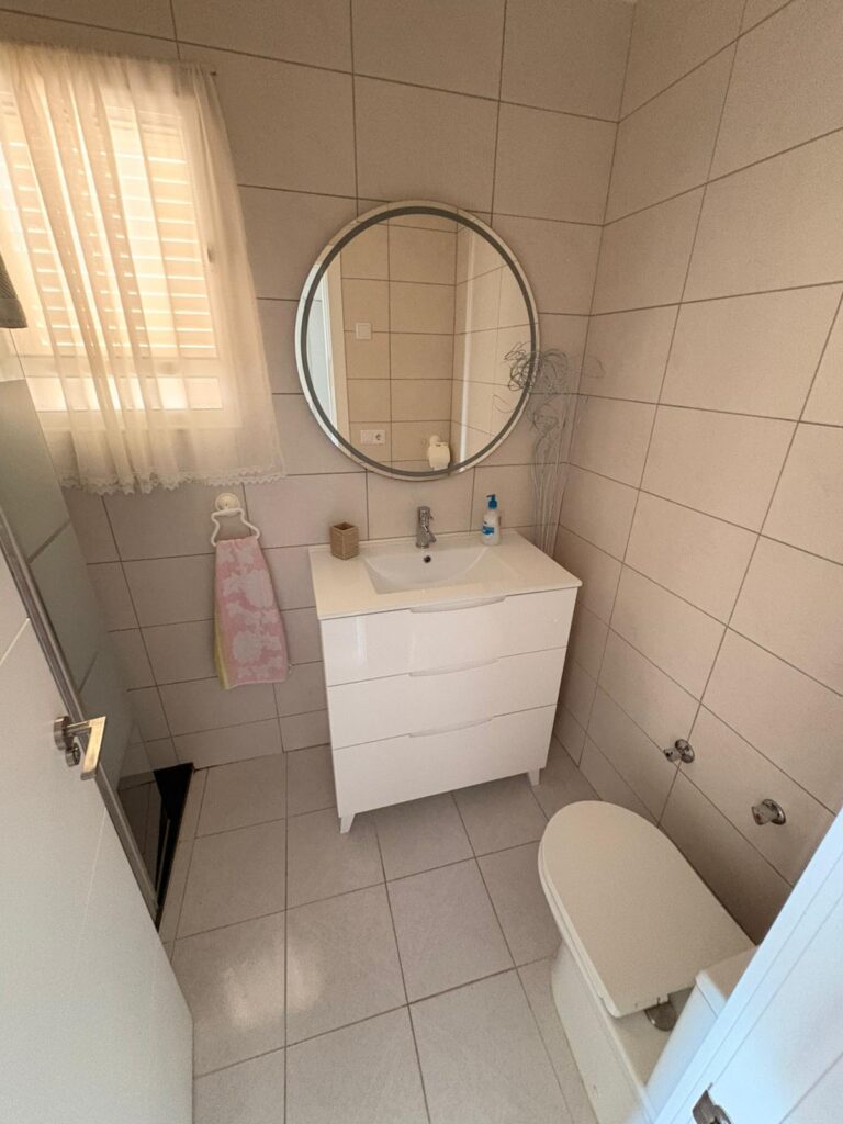 Una pequeña habitación con un lavabo y un inodoro, con un espejo redondo en la pared