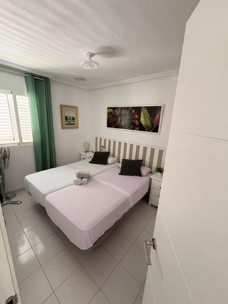 La habitación cuenta con dos camas individuales, una de ellas con una colcha rosa y la otra con una colcha blanca