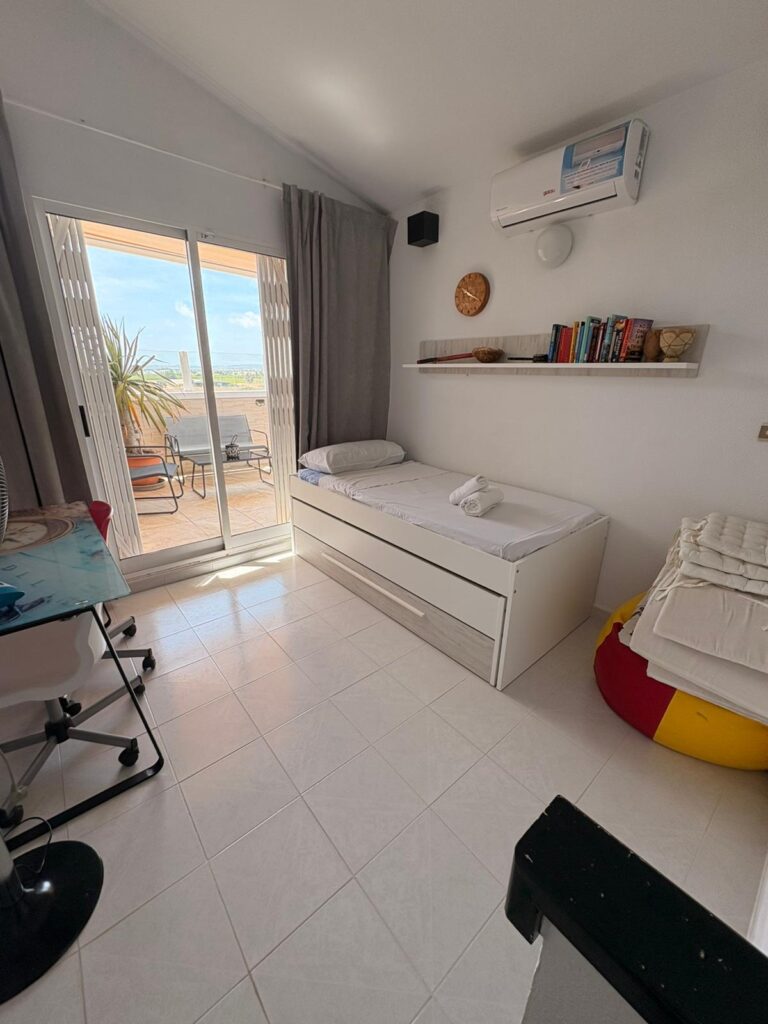 Un dormitorio con una cama individual, un armario con dos cajones, una ventana con cortinas y una vista a la terraza