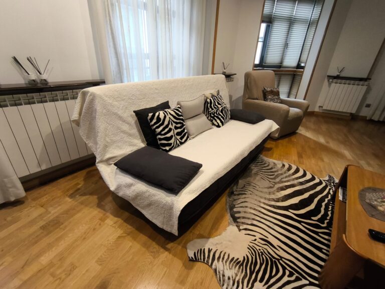 Un sofá con dos cojines zebra y un cojín negro, un sillón de color beige, una alfombra zebra y una mesa de madera