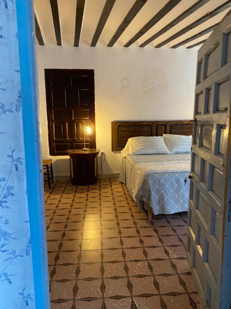 La habitación cuenta con una cama doble, una mesa de noche y una silla. La cama está cubierta con una colcha blanca