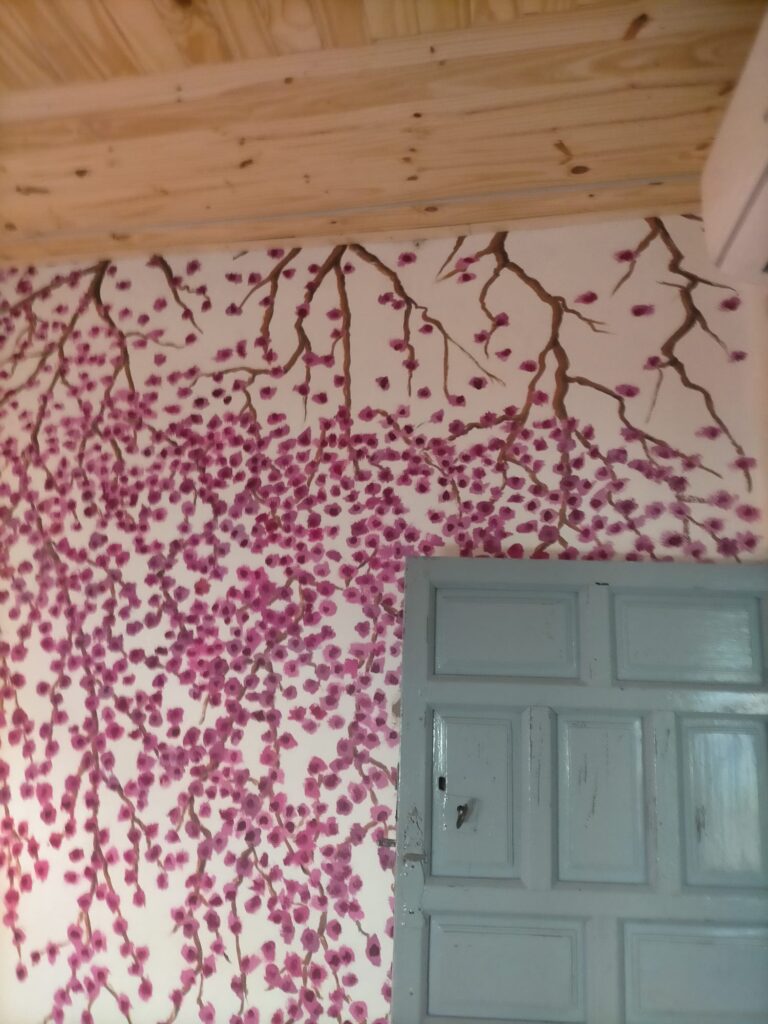 Una pared con un diseño de ramas de árbol con flores, pintado en un color rosa intenso