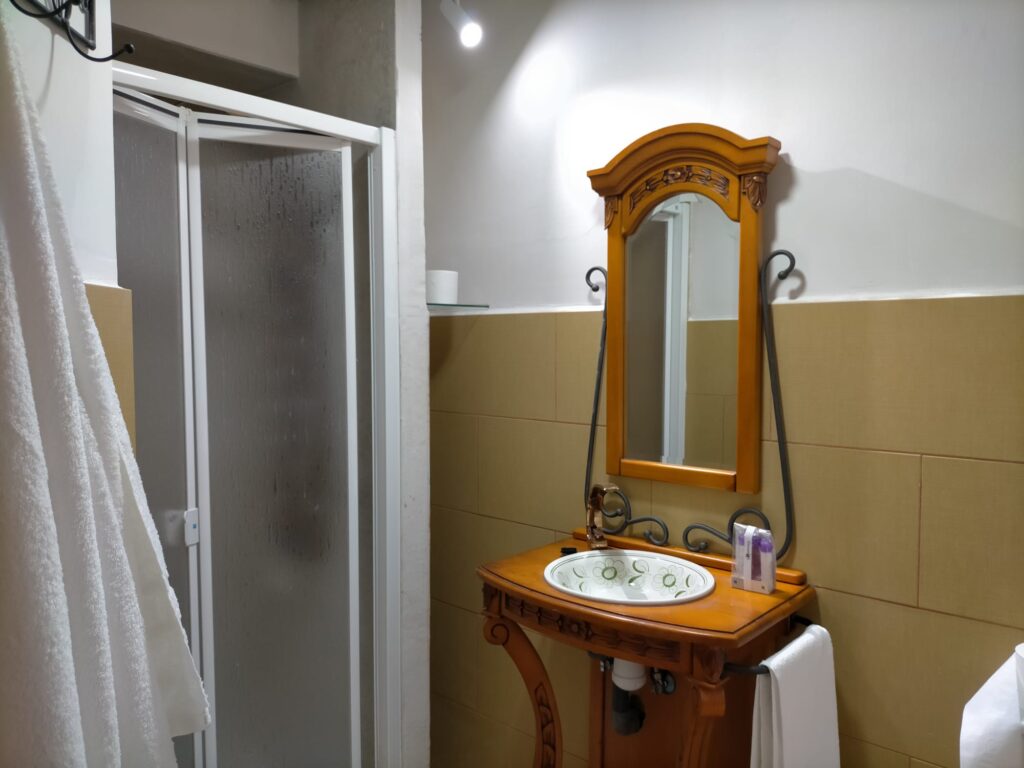 Un baño con un lavabo de madera y un espejo rectangular de madera. El lavabo tiene un fregadero blanco con grifería