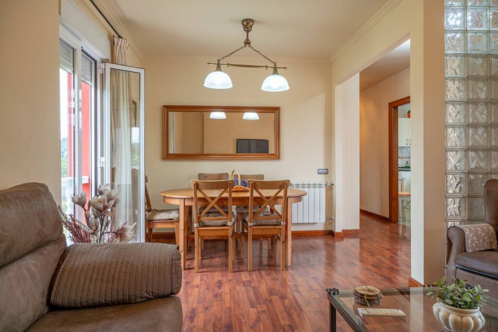 Una sala de estar con una mesa de madera y cuatro sillas, una ventana con cortinas y una puerta de vidrio que da