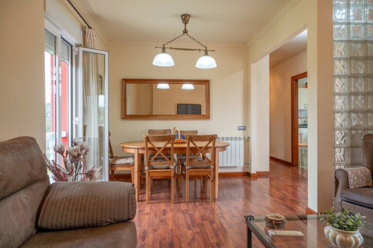 Una sala de estar con una mesa de madera y cuatro sillas, una ventana con cortinas y una puerta de vidrio que da