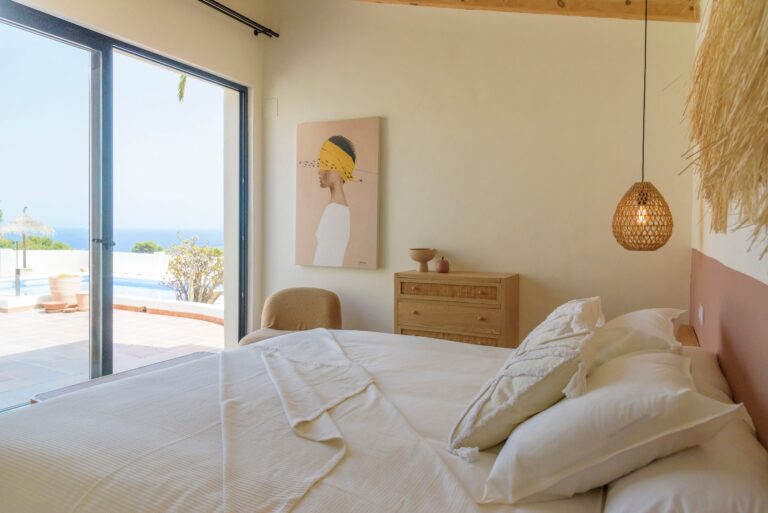 Un dormitorio con una cama doble, una silla y un armario. La cama está hecha con una colcha blanca y dos almohadas