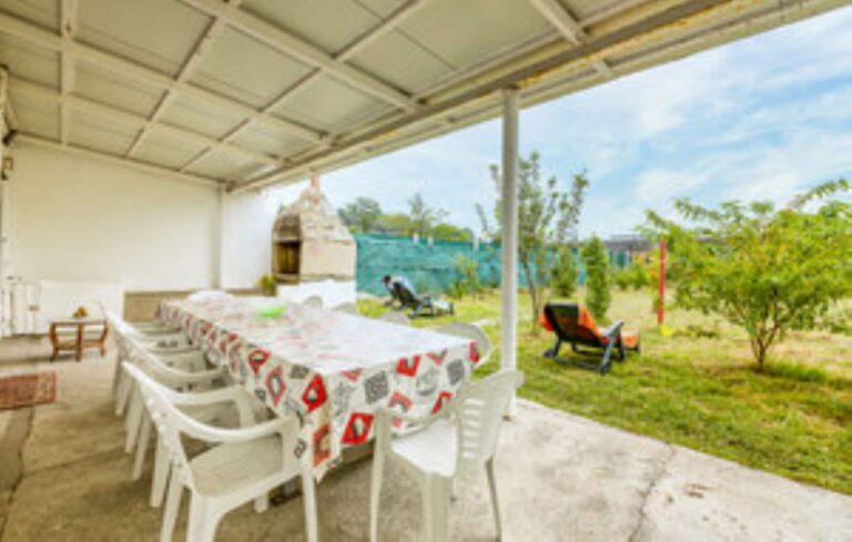 Una terraza con una mesa y sillas de plástico blanco, cubierta por una lona con un diseño de colores rojo, blanco