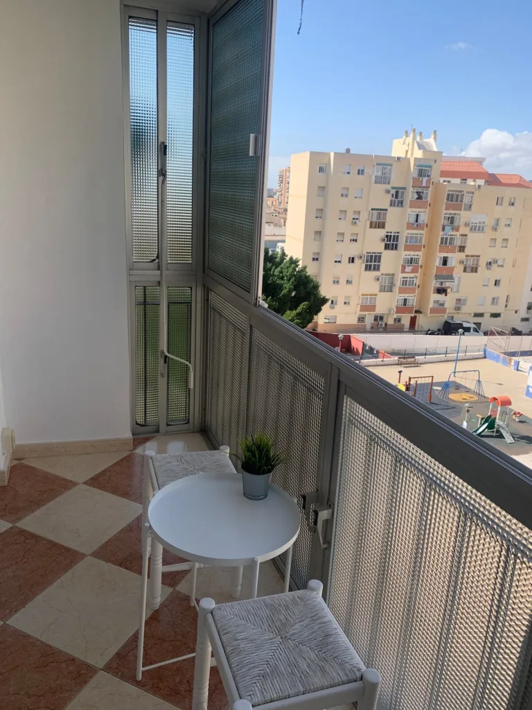 Una terraza con dos mesas y dos sillas, y en el fondo se ve un edificio de apartamentos