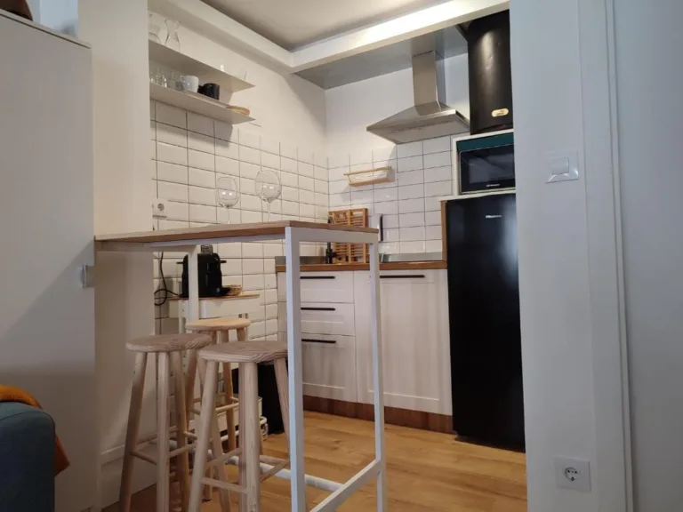 Una cocina con una barra de madera y dos taburetes blancos y un frigorífico negro